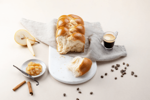 Photo d'une brioche tressée La Boulangère sur une planche de marbre avec une tasse de café à côté.