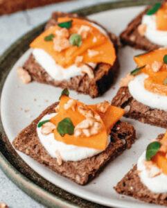 Une assiette avec des Toast seigle & graines, ricotta et kaki