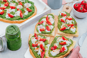 Photo de deux tranches de bruschetta avec du pesto, de la burrata, et des tomates. Sur une planche en bois