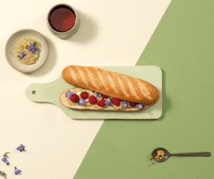 Photo d'une baguette viennoise La Boulangère avec des framboises et des fleurs, au centre ainsi qu'un thé aux fruits rouges.